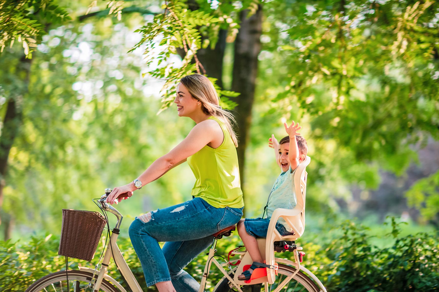 Maman à vélo avec son enfant sur le porte-bagage qui lève les bras au ciel